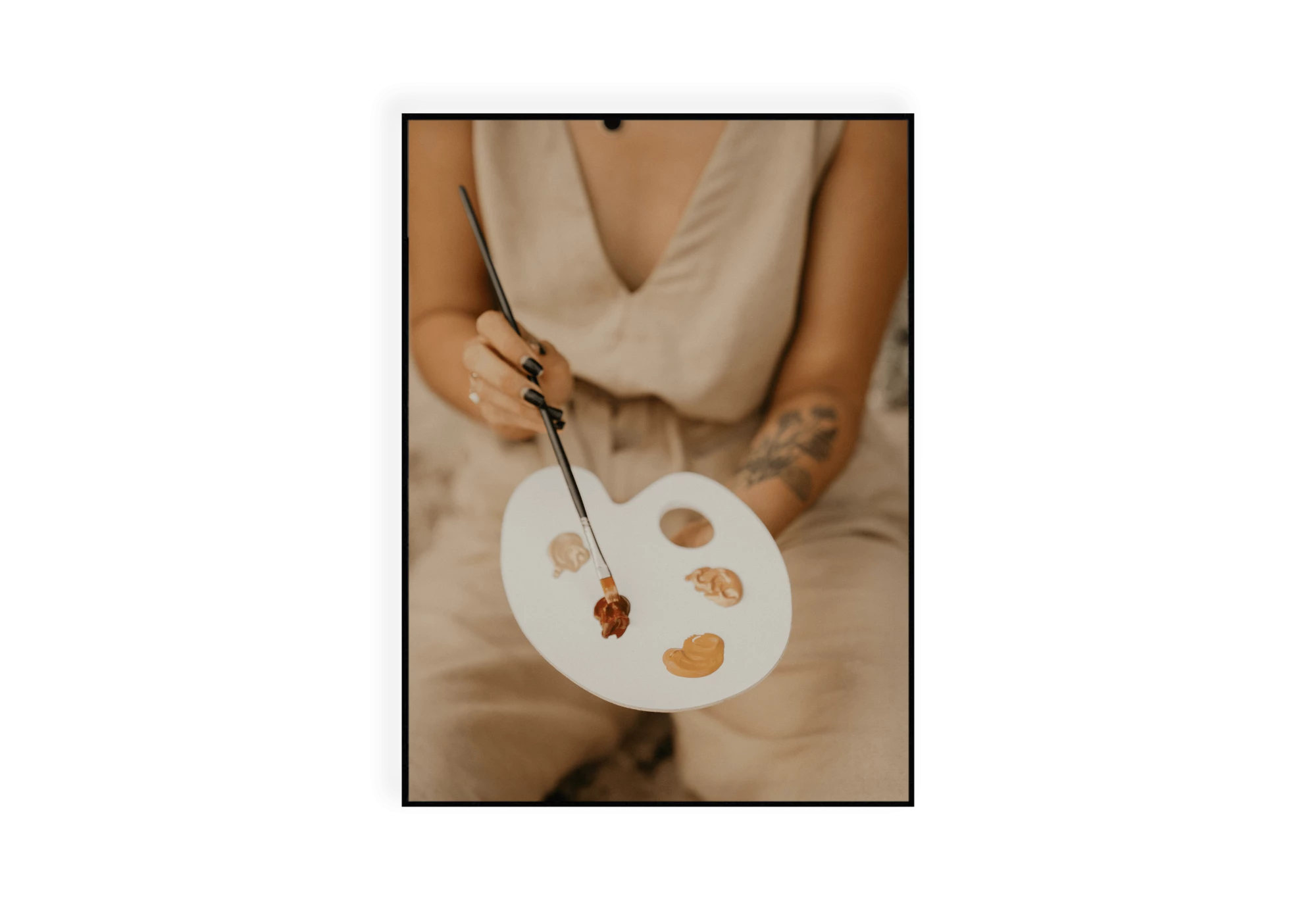 Photographie d'une artiste tenant un pinceau et une palette de peinture aux tons chauds beige, rouille, ocre.