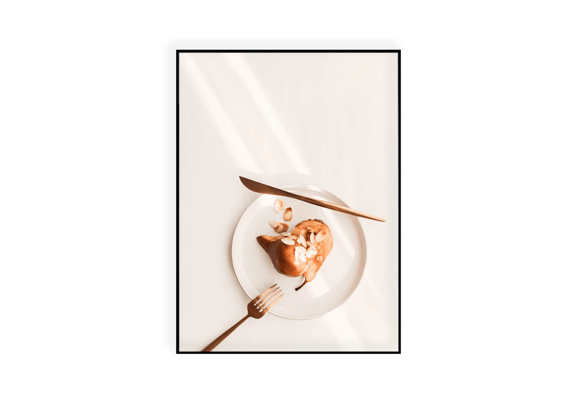 Photographie d'une assiette contenant une poire aux amandes éffilées coupée en deux. Une fourchette et un couteau couleur cuivre sont disposés autour de l'assiette blanche.